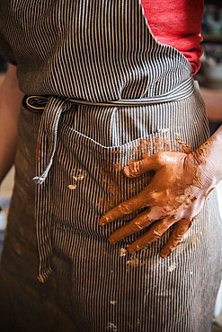 Caucasian woman wiping hands covered with pottery clay on apron