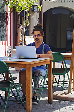 Mixed race man with prosthetic leg using laptop at sidewalk cafe