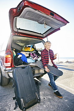 Caucasian man holding skateboard and texting on cell phone