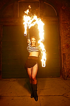 Caucasian woman juggling fire on city sidewalk at night