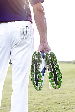 Hispanic man hold golf shoes covered with grass