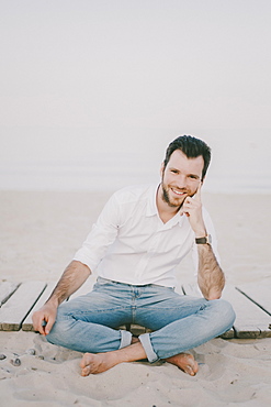 Caucasian man sitting on boardwalk at beach