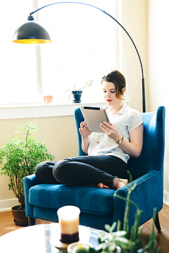 Woman sitting in armchair using digital tablet