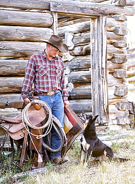 Caucasian man holding saddle and blanket looking at dog