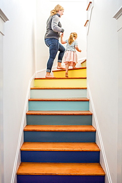 Caucasian mother and daughter climbing multicolor staircase