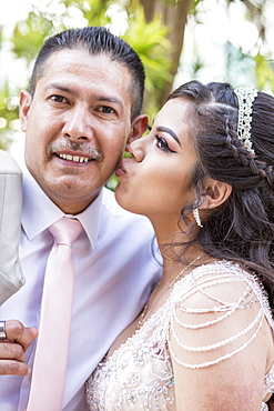 Hispanic girls wearing gown kissing father on cheek