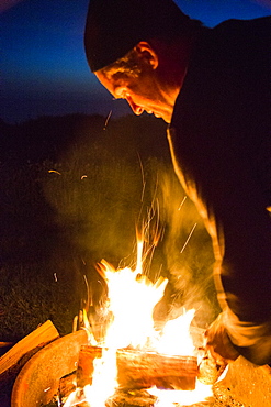 Caucasian man stoking campfire at night