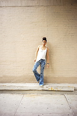 Serious African American woman standing on ledge at brick wall