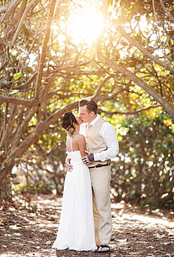 Caucasian bride and groom kissing under trees