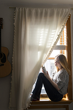 Smiling woman sitting in window using digital tablet