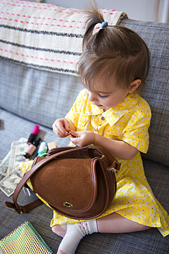 Caucasian baby girl playing with purse on sofa