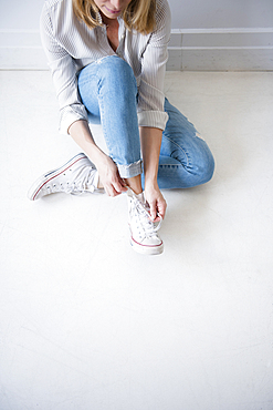 Caucasian woman sitting on floor tying shoelace