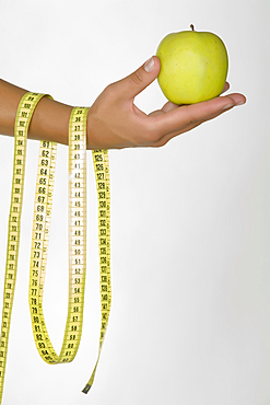 Hand of Caucasian woman holding green apple and measuring tape