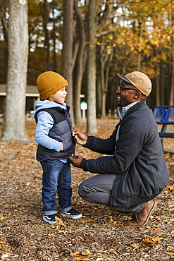 Father zipping vest for son in park