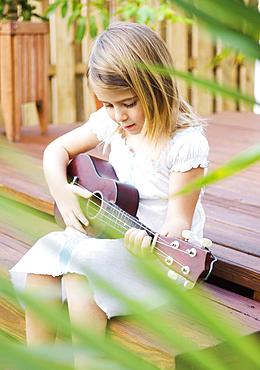 Caucasian girl sitting on patio playing ukulele