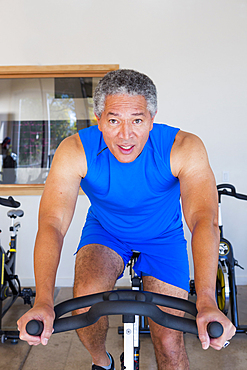 Mixed Race man riding stationary bicycle in gymnasium