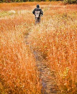 Caucasian man walking on path carrying fishing rod