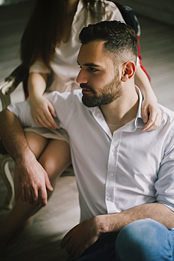 Caucasian man sitting on floor leaning on woman in chair