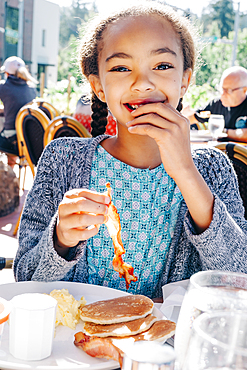 Smiling Mixed Race girl eating breakfast at restaurant