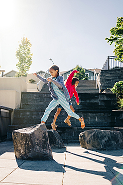 Mixed Race sisters jumping on rocks