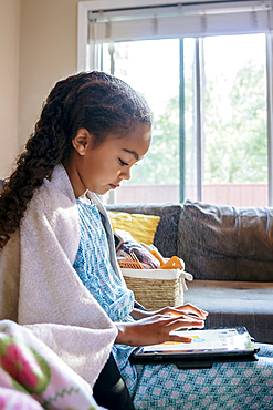 Mixed Race girl using digital tablet on sofa