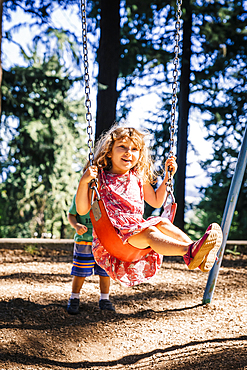 Caucasian boy pushing sister on playground swing