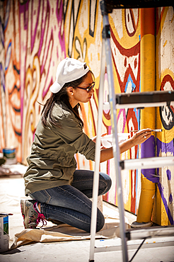 Woman kneeling on tarp painting mural on wall