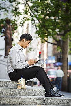 Chinese businessman texting on cell phone during lunch in city