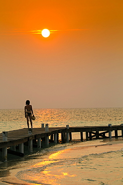 Mixed Race woman standing on ocean dock at sunset