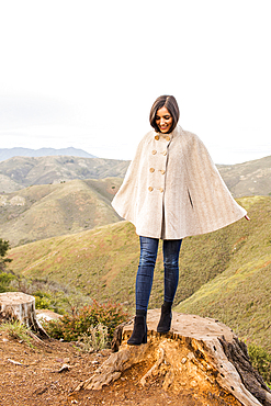 Smiling Indian woman wearing poncho standing on tree stump