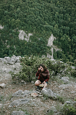 Smiling Caucasian woman crouching on mountain holding pan