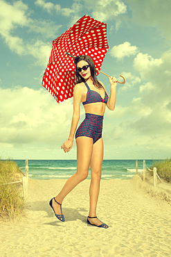 Caucasian woman holding polka-dot umbrella at beach