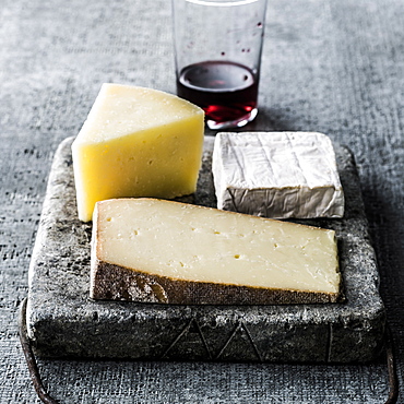 Variety of wedges of cheese on cutting board with red wine