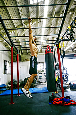 Mixed Race man hanging from bars in gymnasium