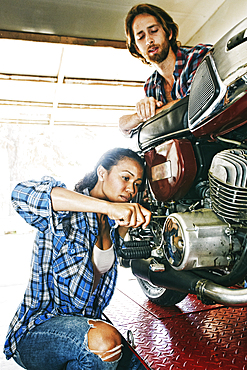 Man watching woman repairing motorcycle in garage