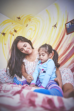 Hispanic mother and daughter on bed looking down