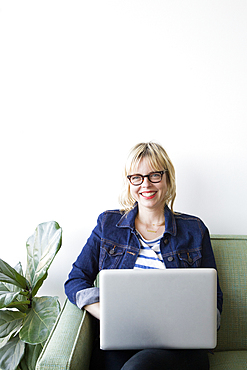 Caucasian woman sitting on sofa using laptop