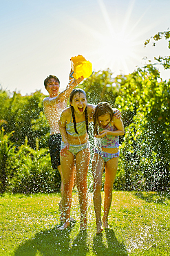 Caucasian boy dumping bucket of water on girls in backyard