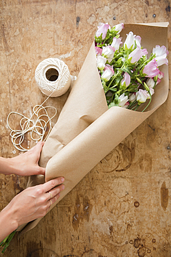 Hands of Caucasian woman wrapping bouquet in brown paper