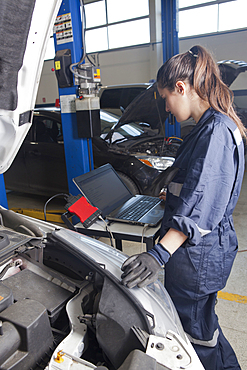 Hispanic mechanic diagnosing car engine with laptop