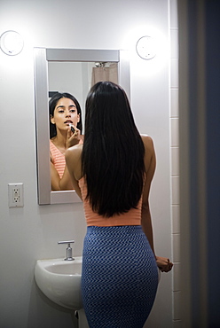 Indian woman applying lipstick in bathroom mirror