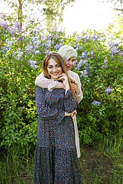 Portrait of young women embracing against lilac bush in garden