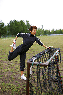 Young woman stretching legs while leaning on mini soccer goal 