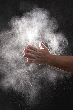 Baker dusting flour off his hands against black background