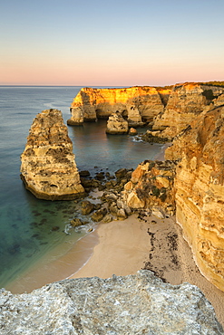 Sunrise on the cliffs and turquoise water of the ocean, Praia da Marinha, Caramujeira, Lagoa Municipality, Algarve, Portugal, Europe