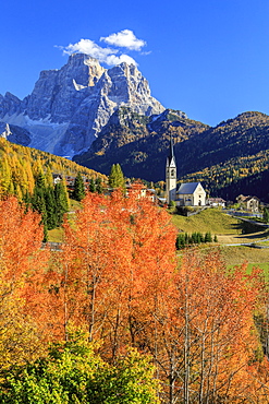 Red and orange trees in front of the tiny church of Selva di Cadore, in the Dolomites, with Mount Pelmo in the background, Veneto, Italy, Europe