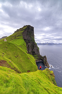 Hiker on cliffs looking to Kallur Lighthouse, Kalsoy Island, Faroe Islands, Denmark, Europe