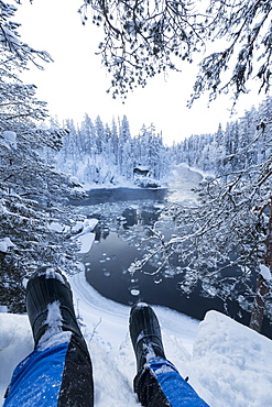 Hiker rests on the snow above Myllykoski rapids, Juuma, Oulanka National Park, Kuusamo, Lapland, Finland, Europe