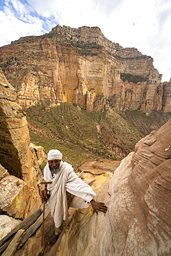 Ethiopian priest leaning on steep rocks leading to Abuna Yemata Guh church, Gheralta Mountains, Tigray Region, Ethiopia, Africa