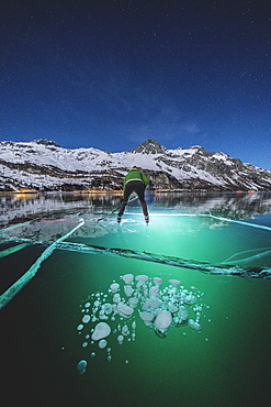 Man skating on frozen Lake Sils lit by head torch at night, Engadine, canton of Graubunden, Switzerland, Europe